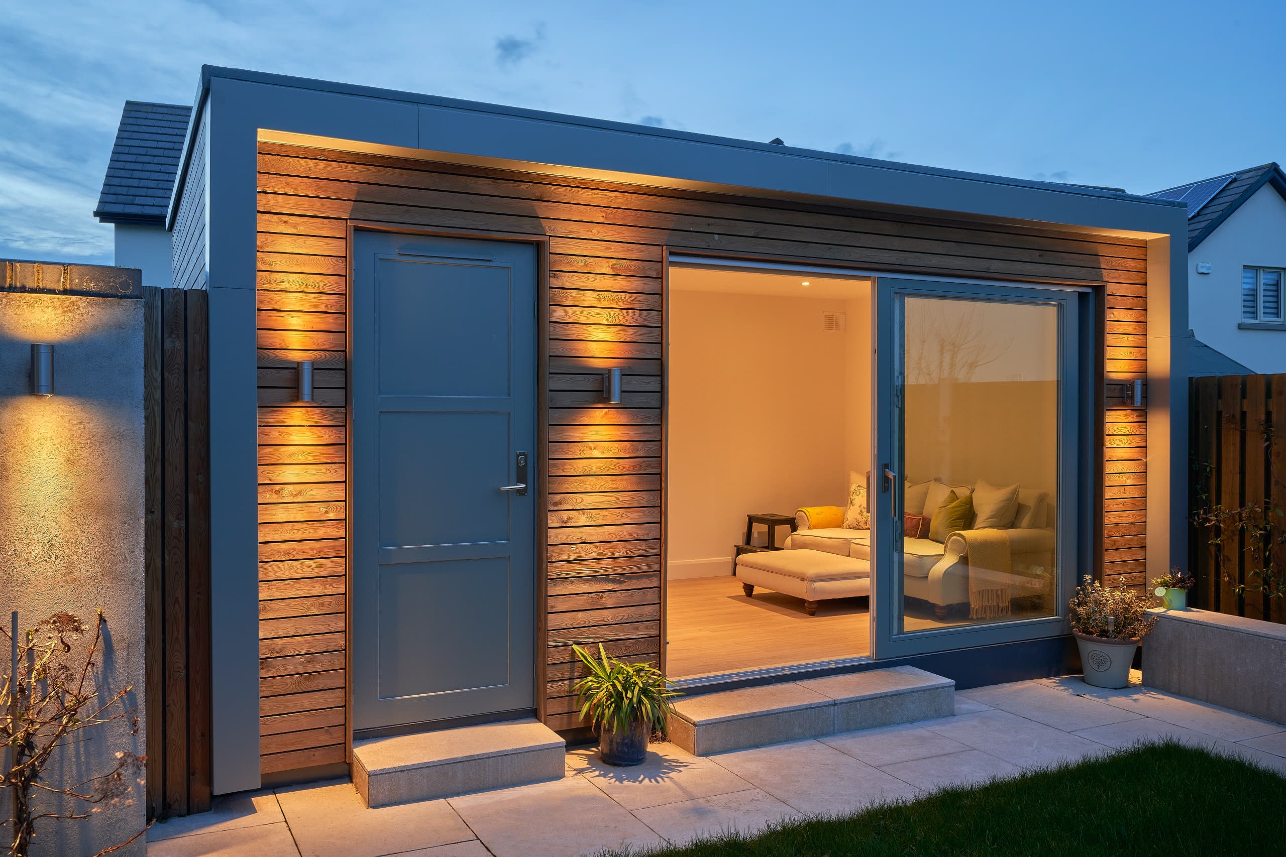 A cedar-clad garden room by Shomera in Barnwell, Dublin, uplit at dusk with the lounge glowing through its sliding doors