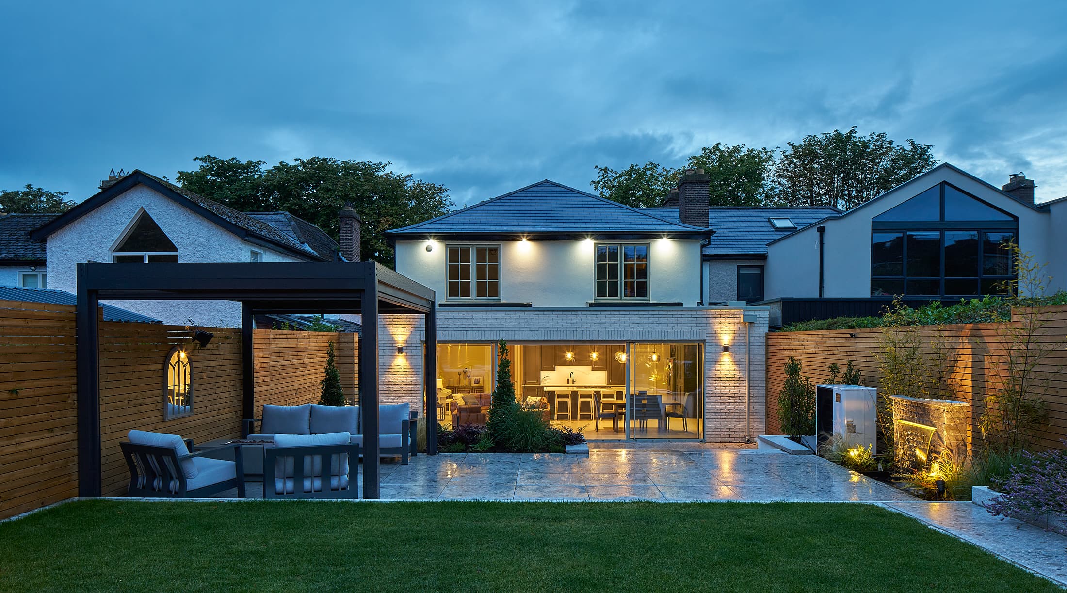 Two-storey extension and home renovation on Griffith Avenue, Dublin, by Shomera, lit at dusk above a pergola patio and lawn