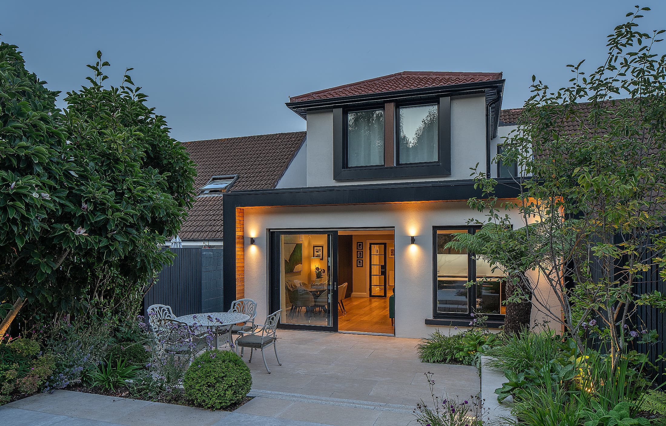 Rear extension to a renovated dormer bungalow in Hillside, Dublin by Shomera, lit at dusk with a dining patio and garden