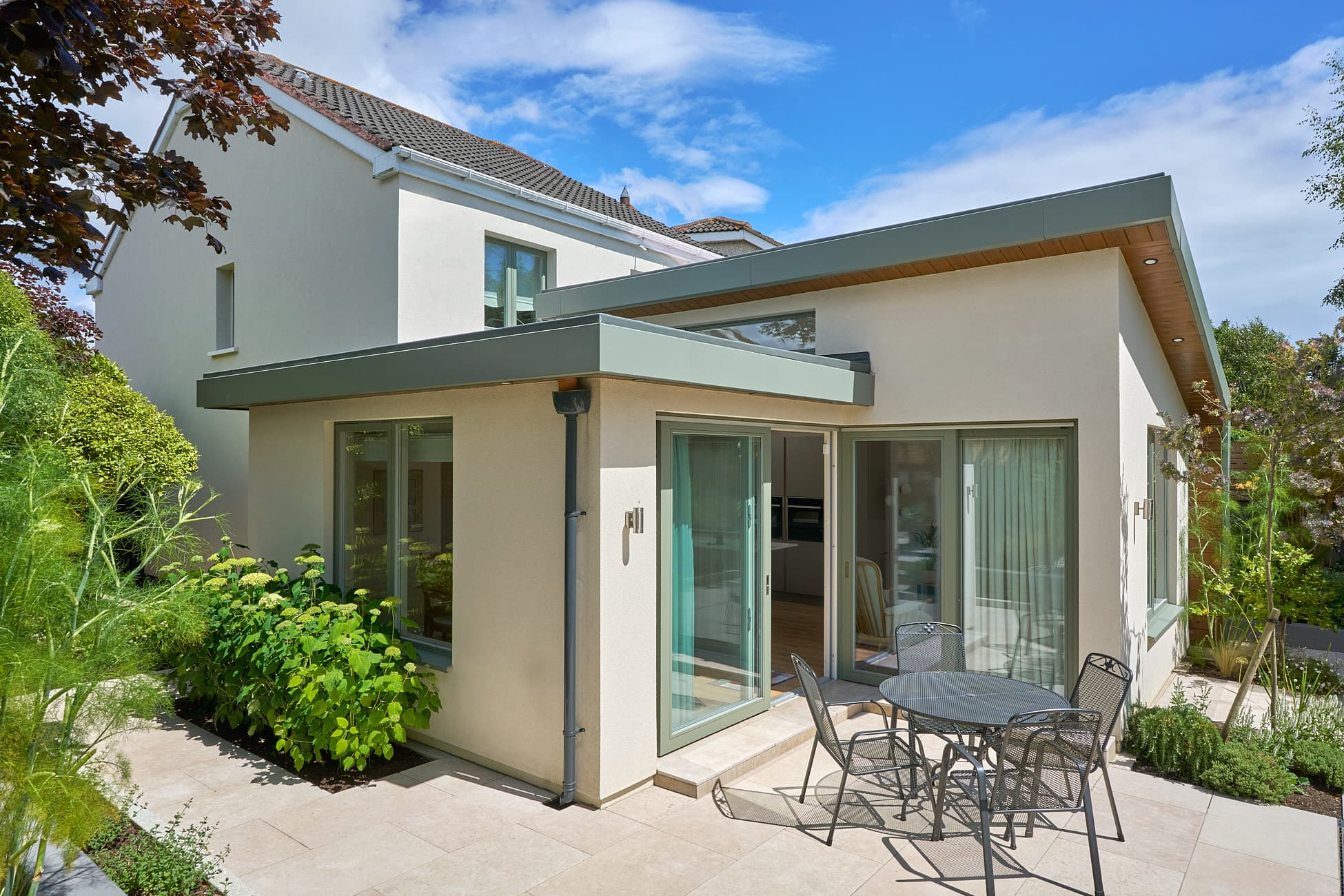 Rendered side and rear extension on Navan Road, Dublin 7, with a green fascia and sliding doors onto a patio, by Shomera