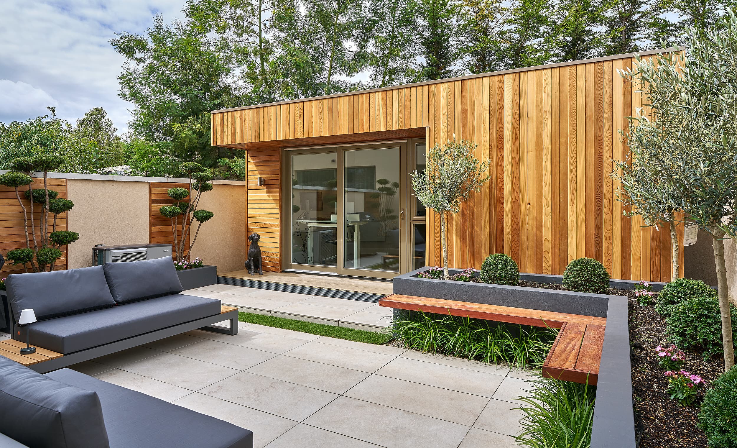 A cedar-clad garden room gym and sauna by Shomera in Monterey, South Dublin, beside a paved terrace with built-in seating