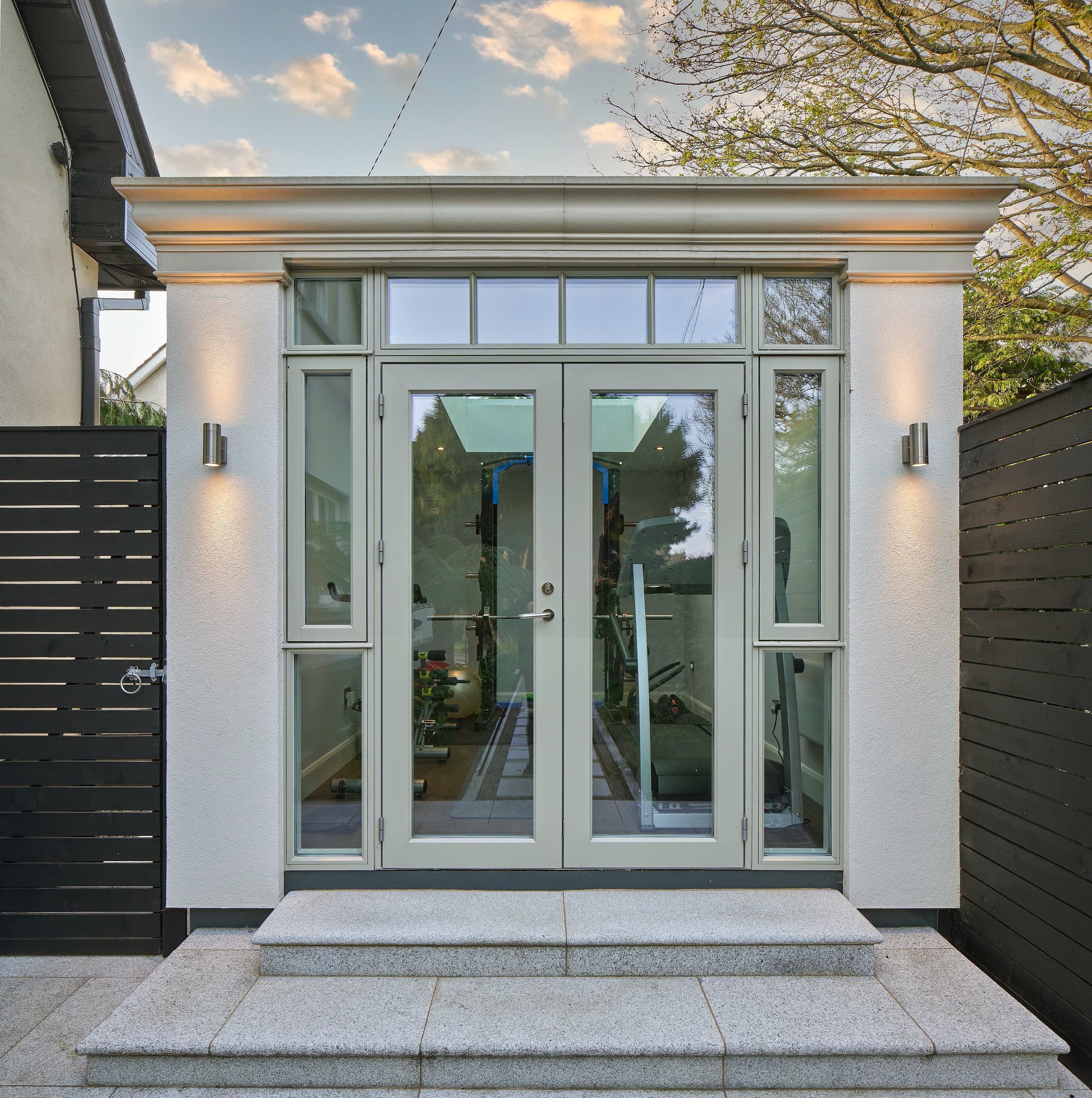Orangery-style garden room used as a home gym in Dublin, with glazed double doors, rendered pilasters and granite steps