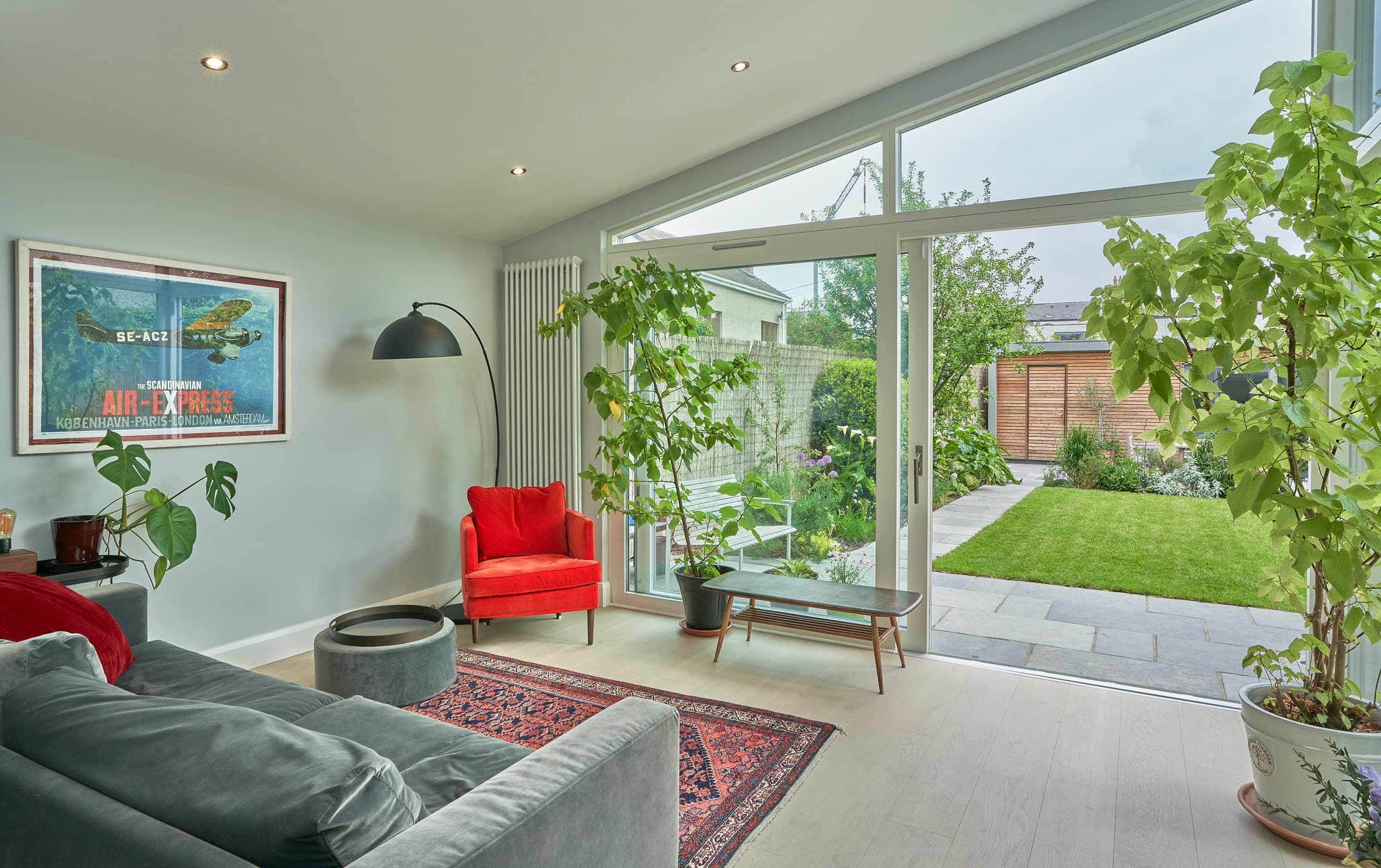 Living space in a rear extension in Dartry, Dublin, its full-height glazing opening onto the lawn and a timber-clad garden building, by Shomera