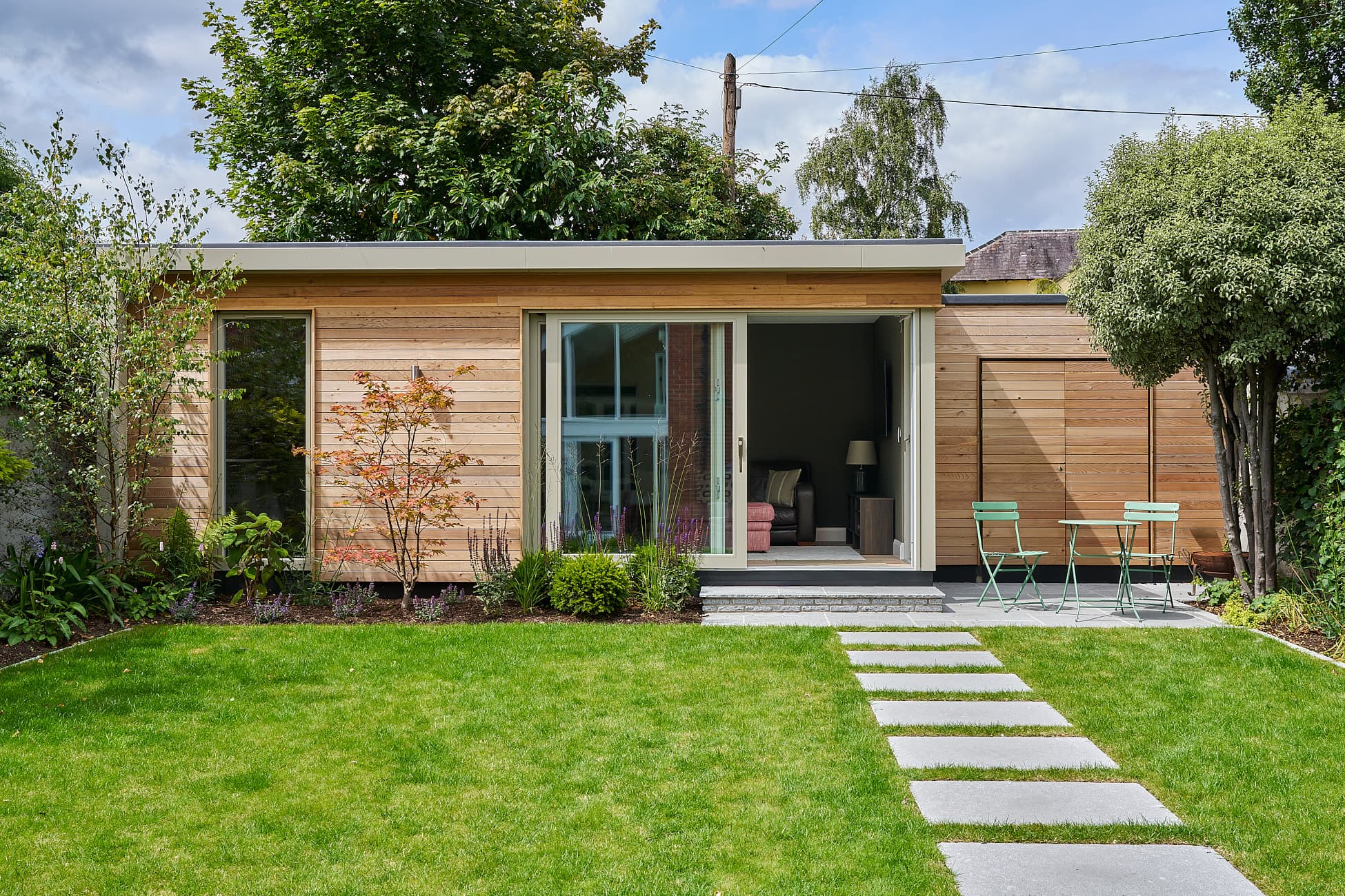 A cedar-clad Shomera garden room on Templemore Avenue, Dublin, its sliding doors open onto a lawn and stepping-stone path