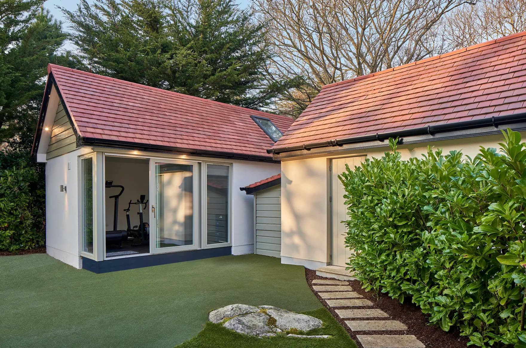 A white rendered building with a tiled pitched roof and glass doors, used as a home gym
